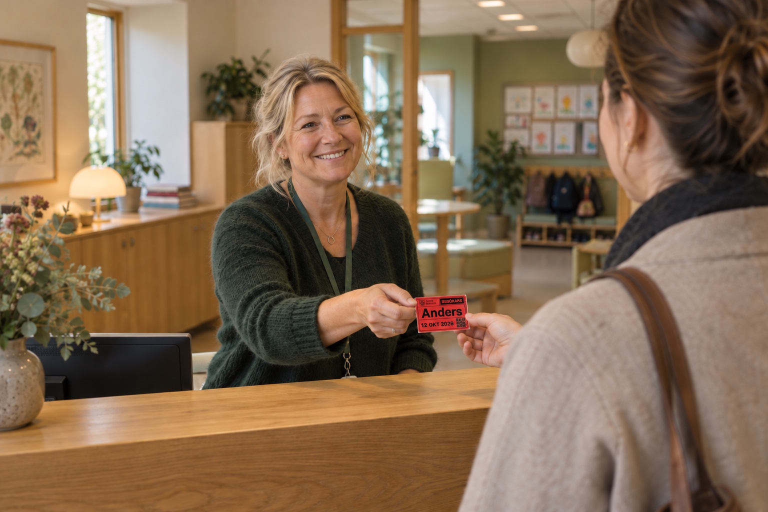 En receptionist välkomnar en besökare med en röd besöksetikett med Sunne kommuns logotyp, namnet Anders, datum och QR-kod.